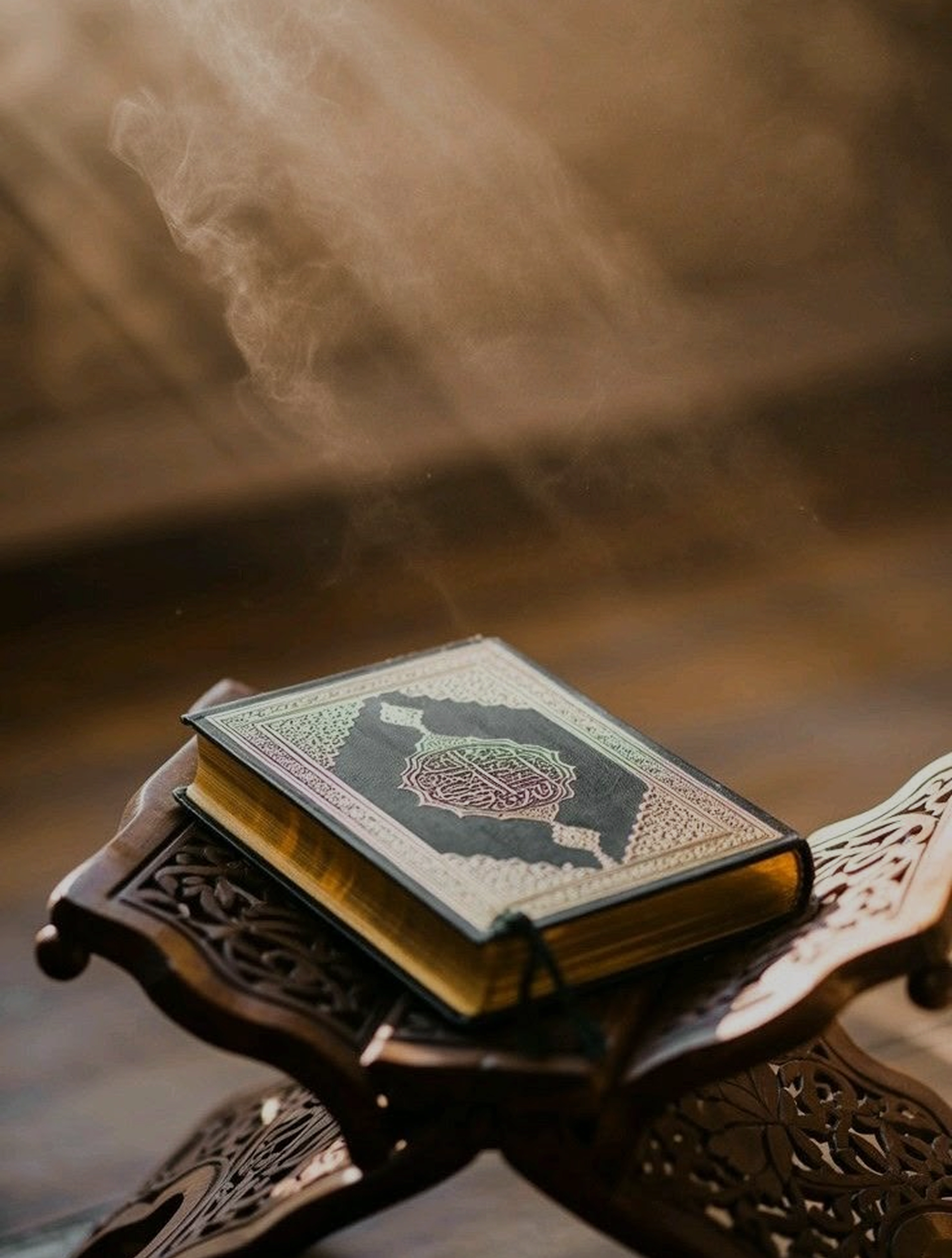 A warm, out-of-focus photograph of an open Qur'an resting on a wooden rehal.
