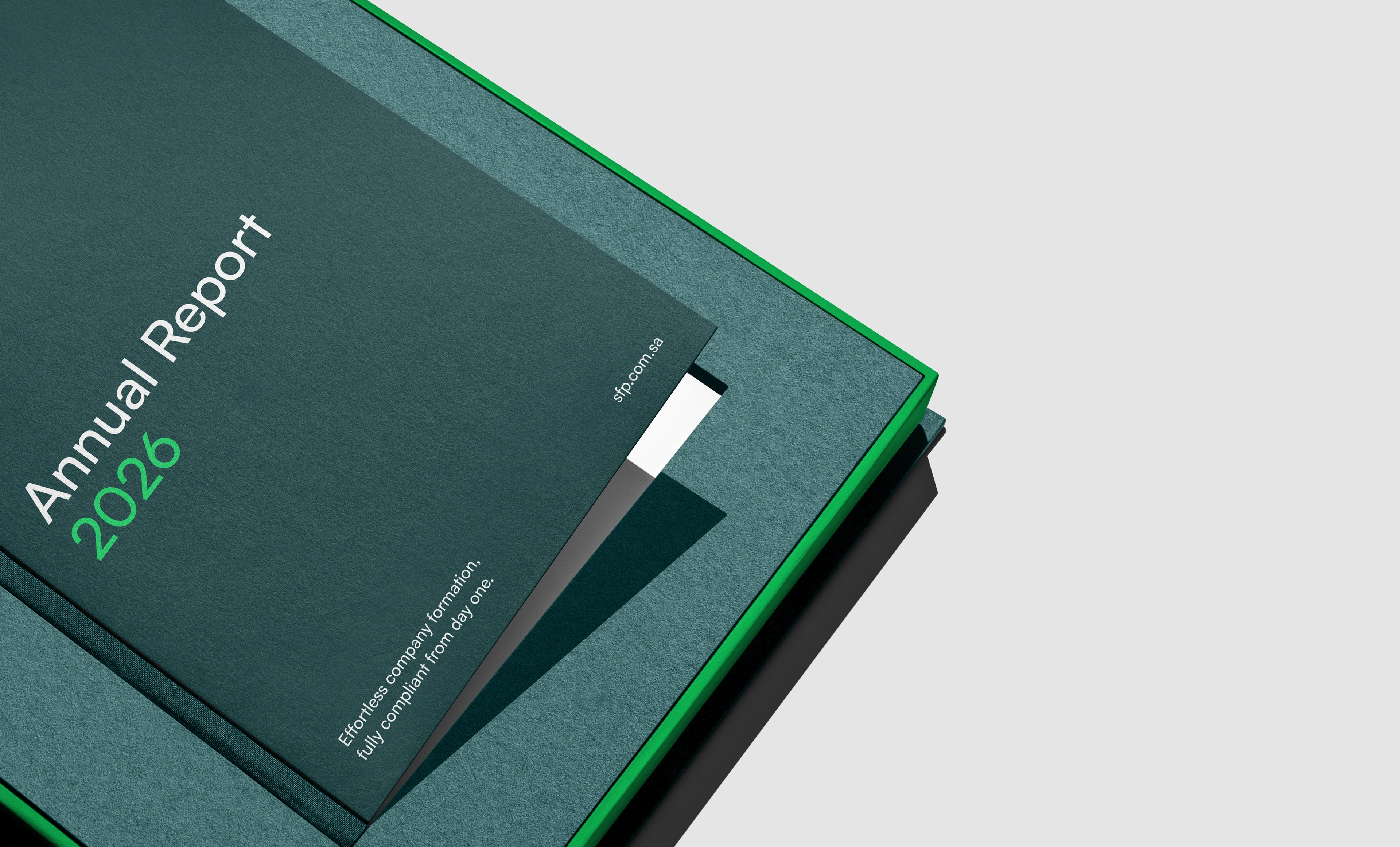 A tight corner crop of a dark teal Annual Report 2026 hardcover resting on a teal slipcase with a bright green rim, the year set in green beside a white bookmark ribbon, with the title running off the left edge of the frame.