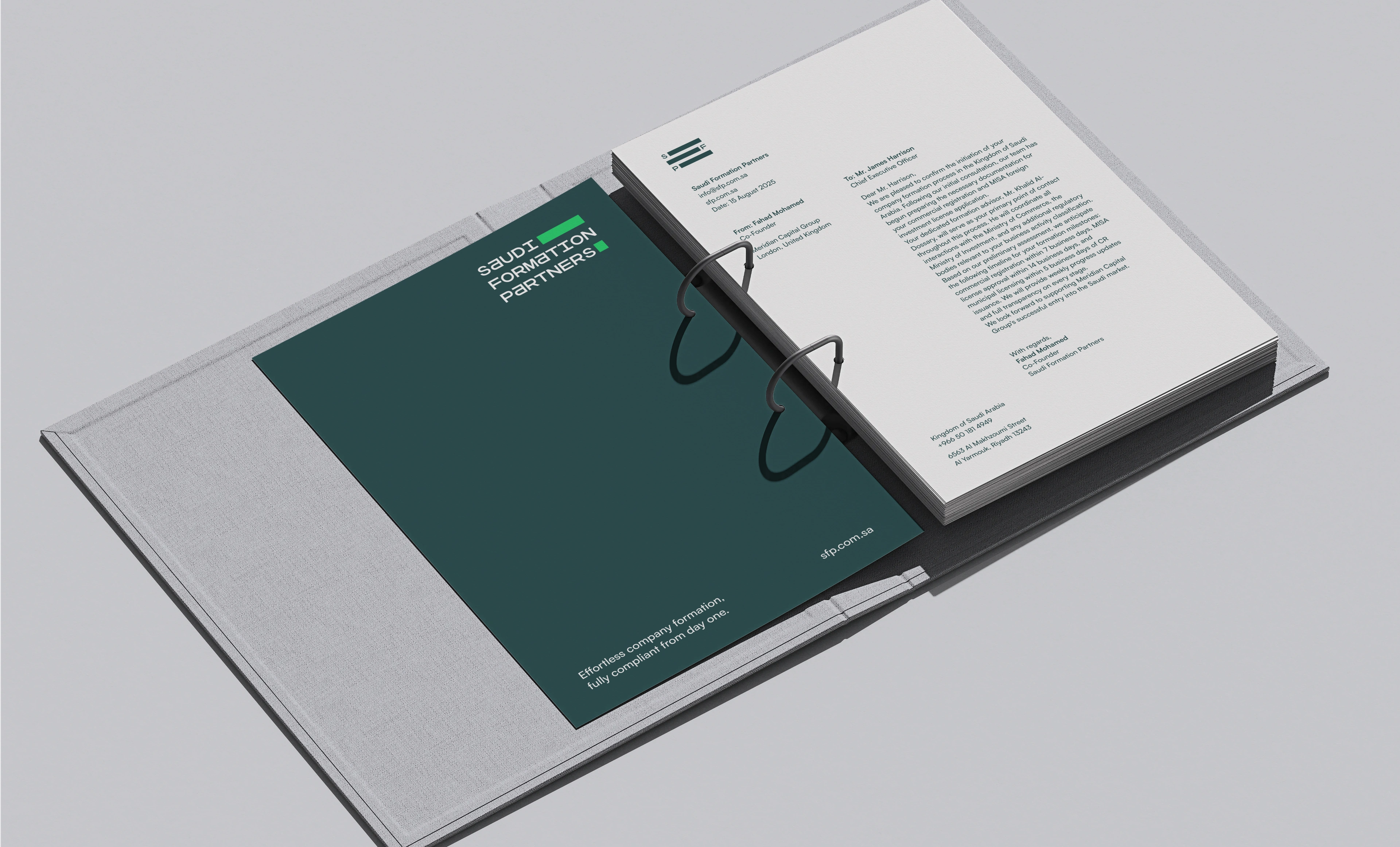 An open two-ring linen binder lying flat on a grey surface, with a punched stack of cream Saudi Formation Partners letterhead pages on its right leaf and a loose dark teal card printed with the company tagline resting on the inside front cover at the left.