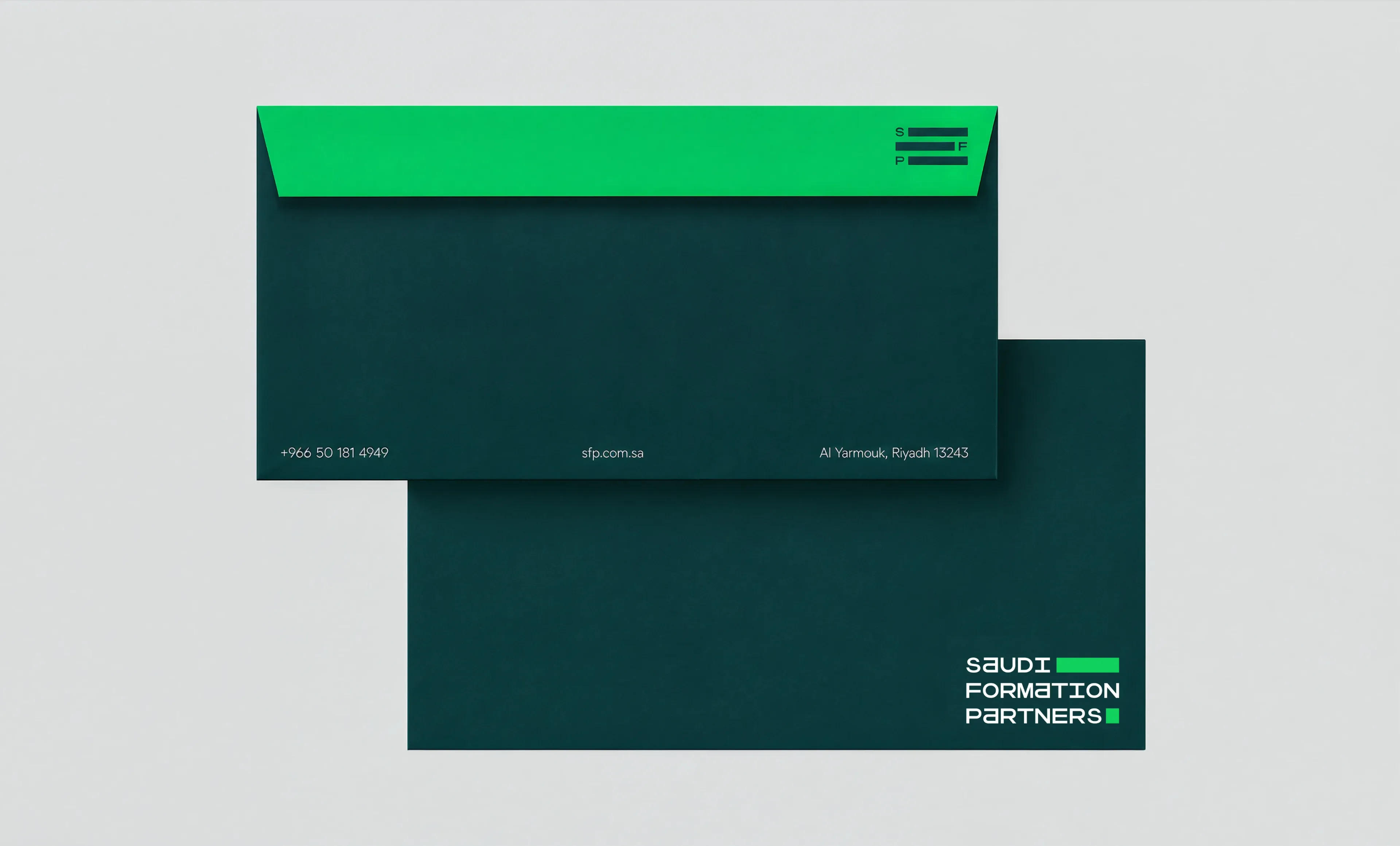 Two dark teal envelopes on a pale neutral ground, one face up with a malachite green flap and a line of contact details along its foot, the other showing the Saudi Formation Partners wordmark, with a printed card beside them.