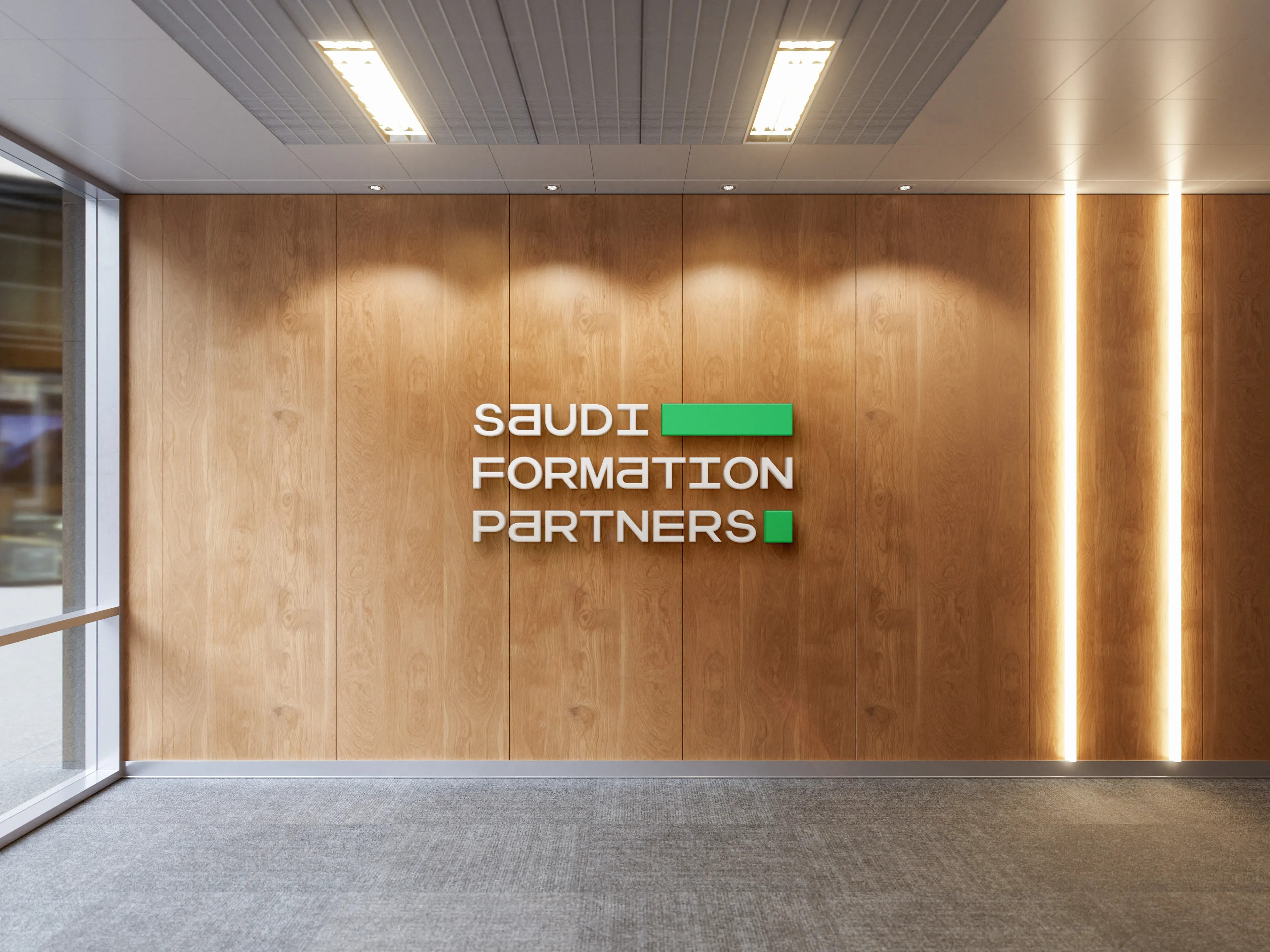 An office reception interior where dimensional white Saudi Formation Partners lettering is mounted on a slatted wood wall, lit by downlights, with glazing along the left edge.
