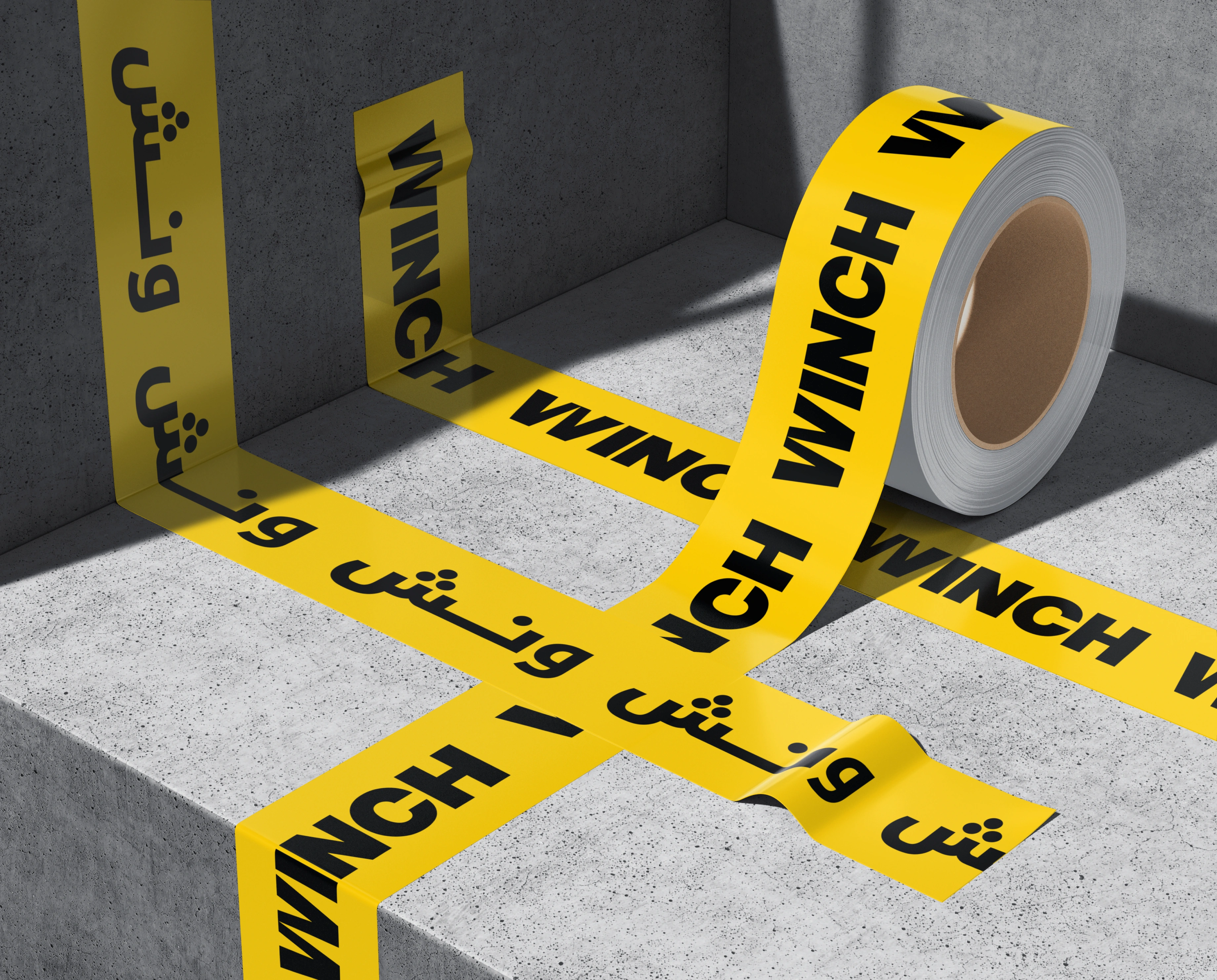 A roll of yellow WINCH barricade tape printed with repeating Latin WINCH and Arabic ونش lettering, the tape crossing a grey concrete step in hard sunlight with the roll resting behind it.