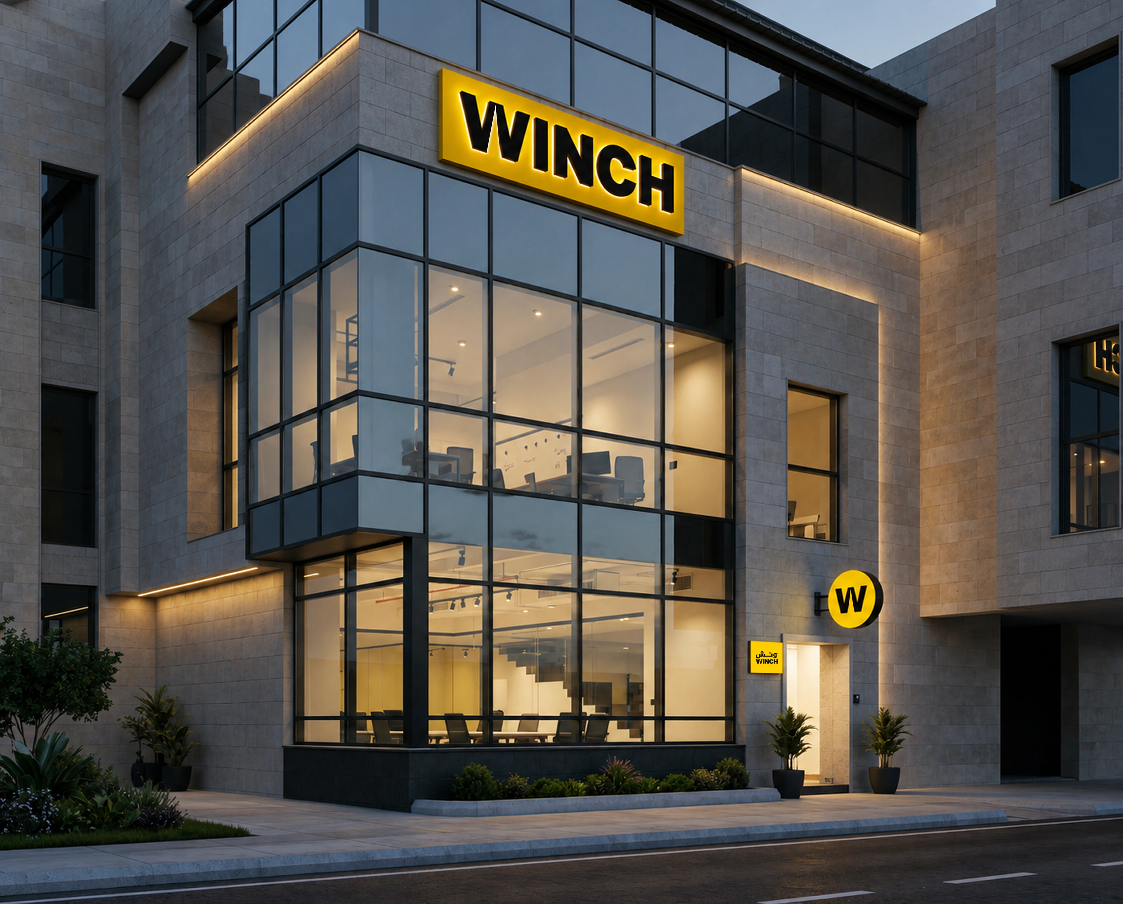 The glass-and-stone facade of an office building at dusk, with an illuminated yellow WINCH fascia sign above the glazing, a round yellow W disc sign beside the entrance and warm light behind the windows.