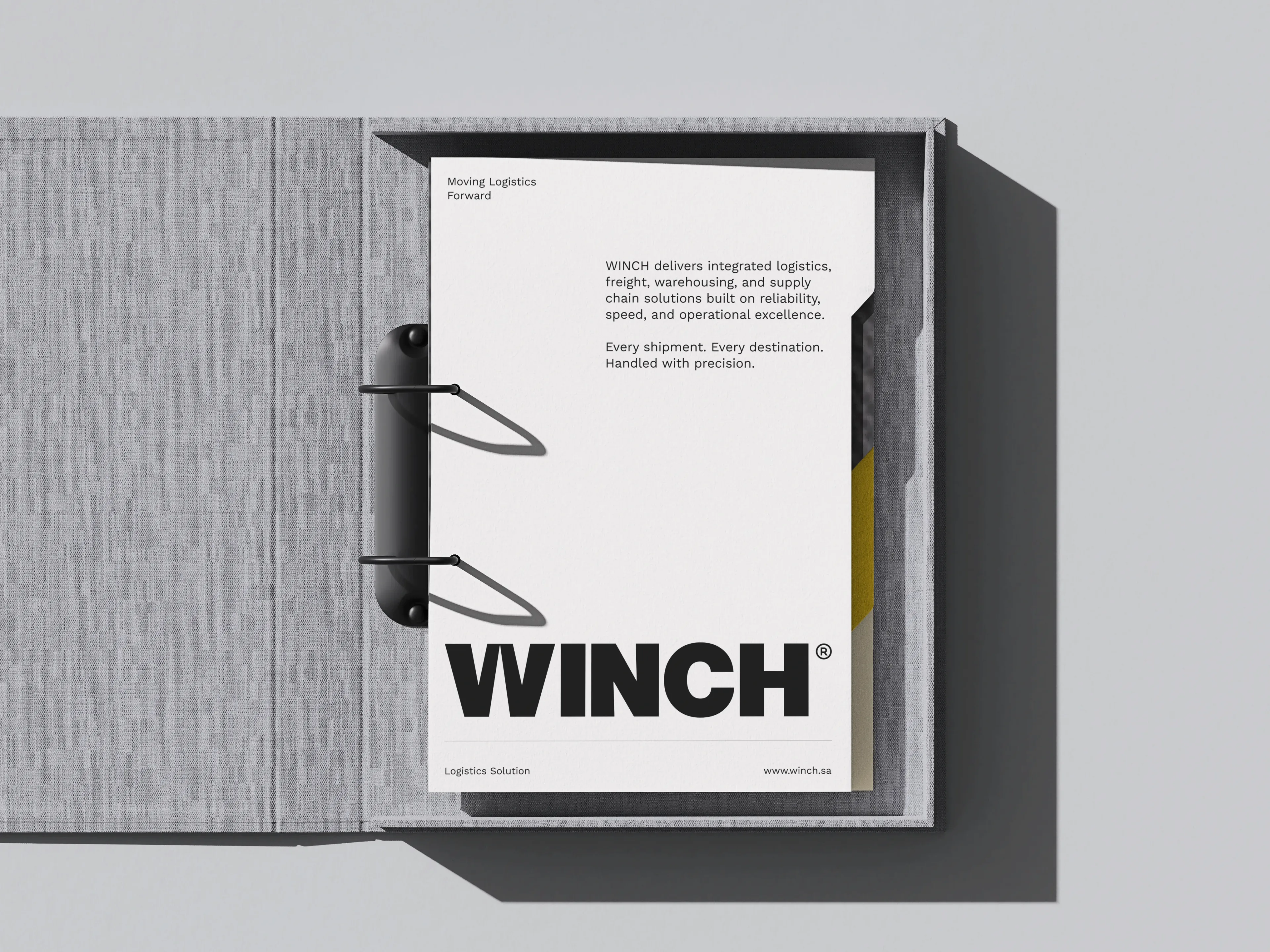 A grey cloth ring binder opened flat on a printed WINCH letterhead sheet headed Moving Logistics Forward, its body copy describing integrated logistics, freight and warehousing services above the WINCH wordmark and the footer Logistics Solution and www.winch.sa.