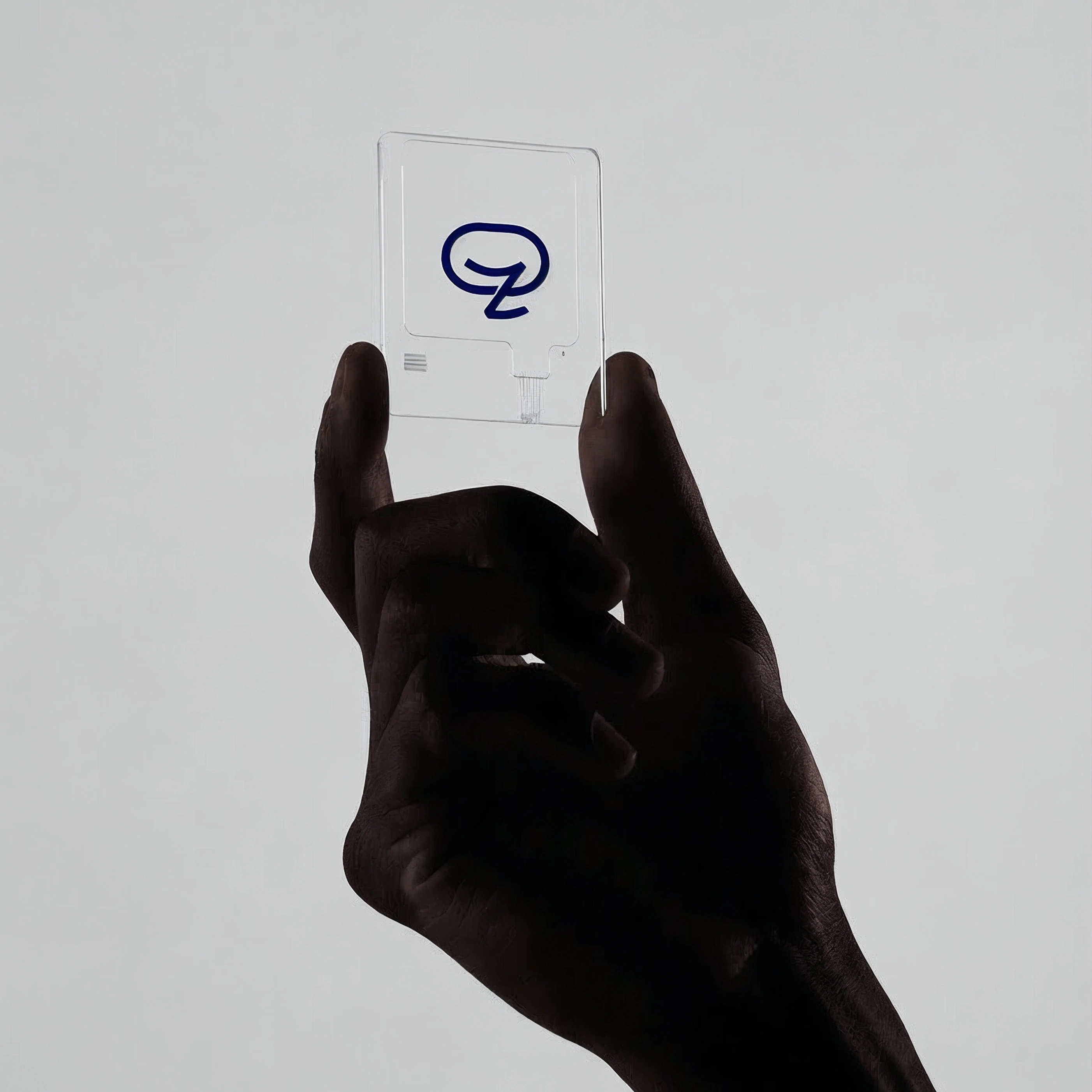 A hand entering from below holds a translucent frosted acrylic card embossed with the navy Zakichat mark against a pale grey studio sweep.