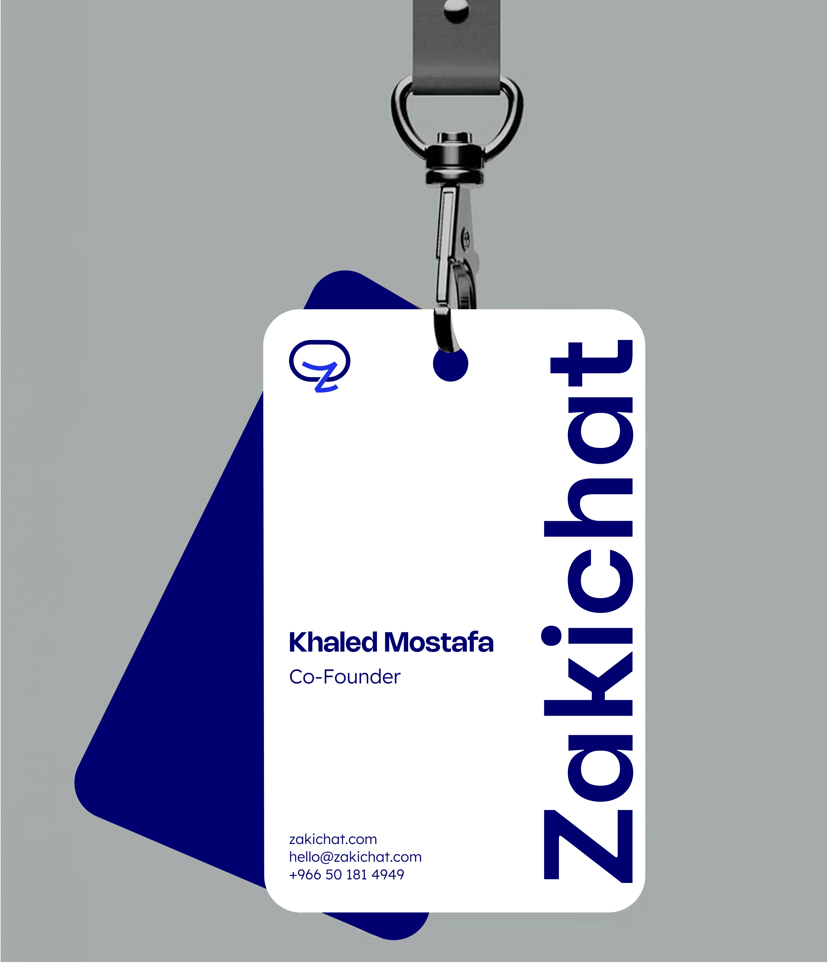 A white Zakichat ID badge on a metal clip over a flat grey-blue ground, printed with the mark, a large vertical Zakichat wordmark and the name Khaled Mostafa, Co-Founder, with a navy card angled behind it.